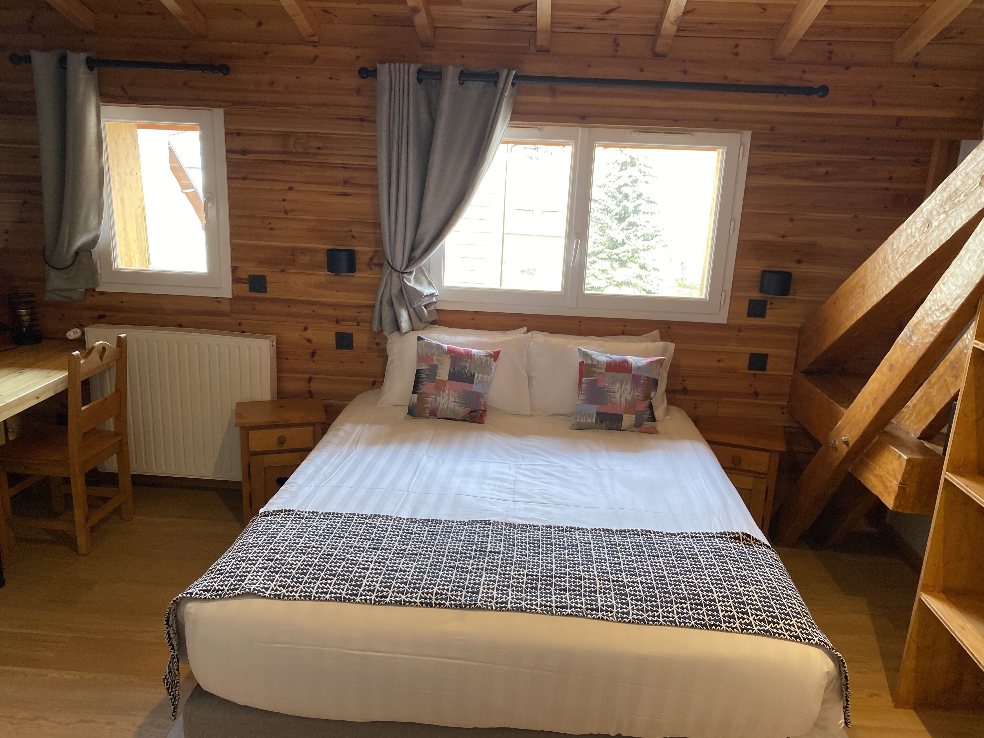 A cozy wooden cabin room with a bed, a desk, and a window with curtains.
