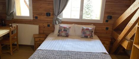 A cozy wooden cabin room with a bed, a desk, and a window with curtains.