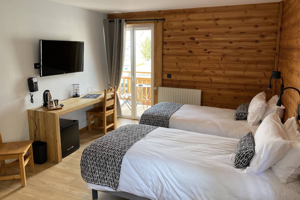 A hotel room with two beds, a desk with a chair, a television, and a window with curtains.
