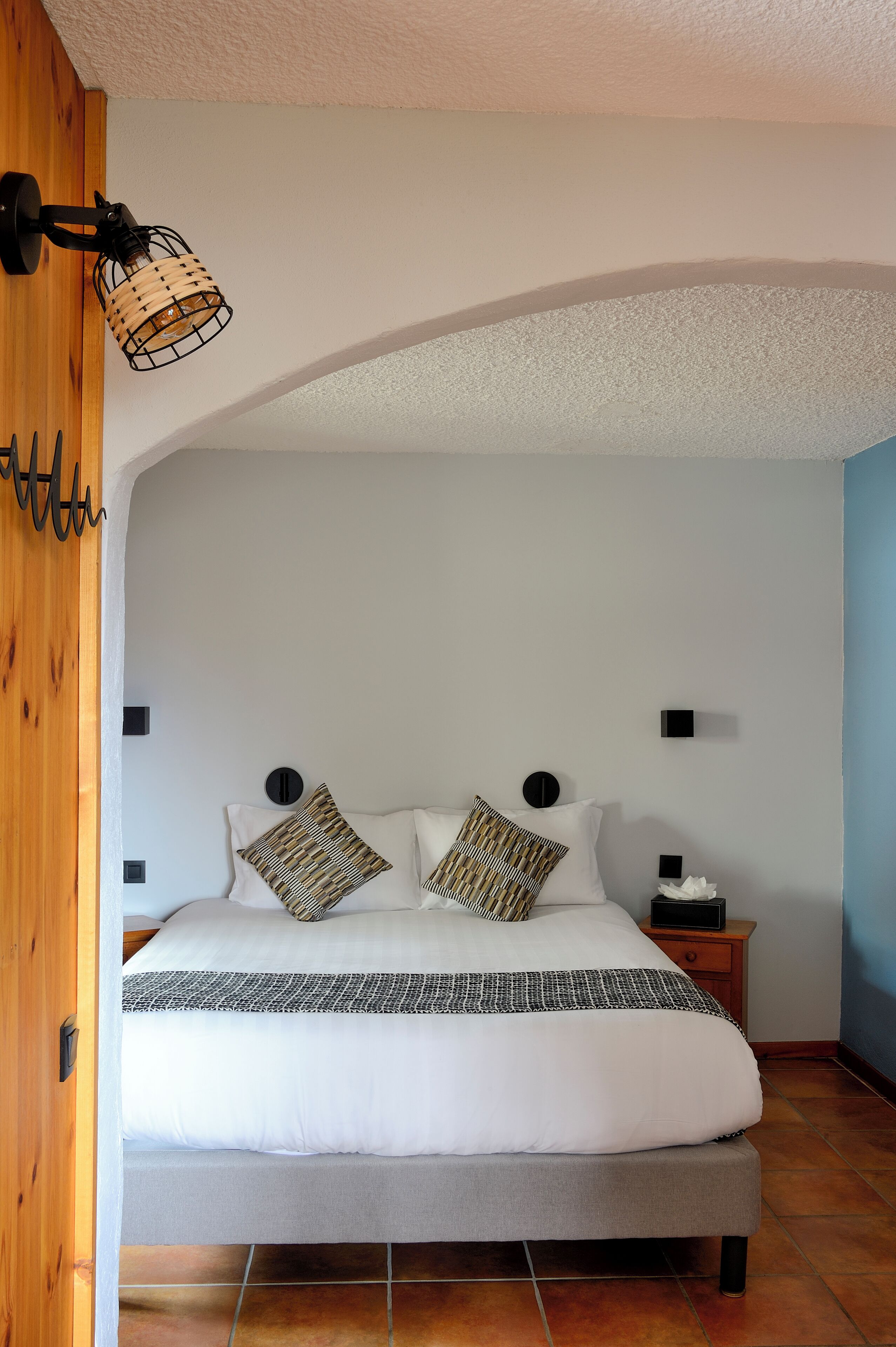 Un dormitorio con cama, almohadas, una mesita de noche y un aplique de pared.