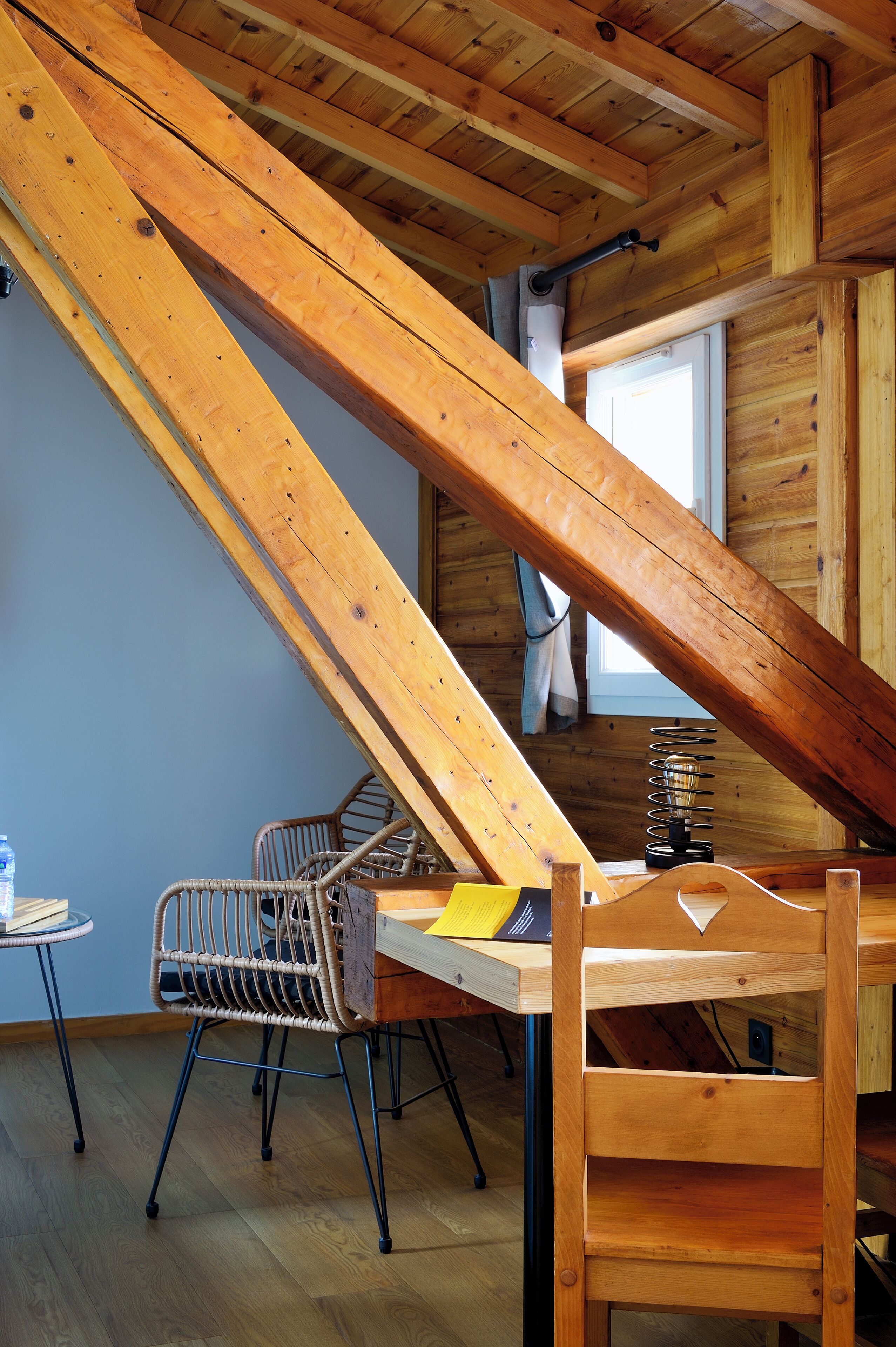Un interior de madera con techo inclinado, una mesa, sillas y un ventanal.