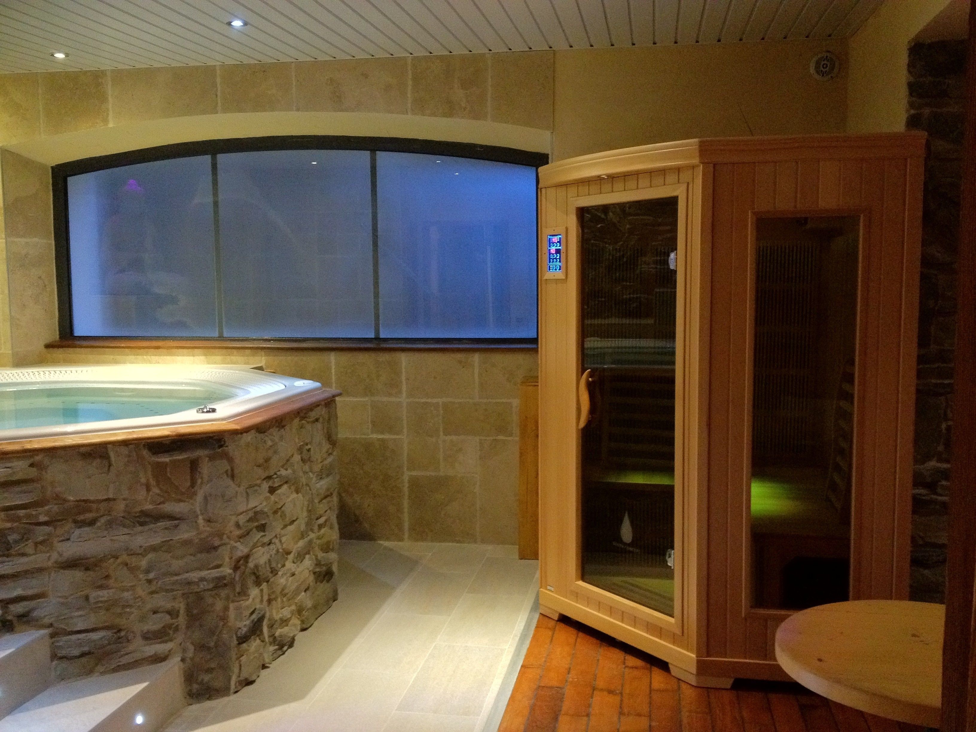 Een spa-ruimte met een stenen badkuip, een houten sauna en een groot raam.