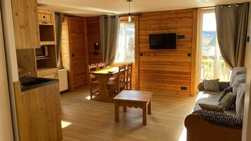 Un interior de madera con una mesa de comedor, sillas, un sofá y un televisor montado en la pared.