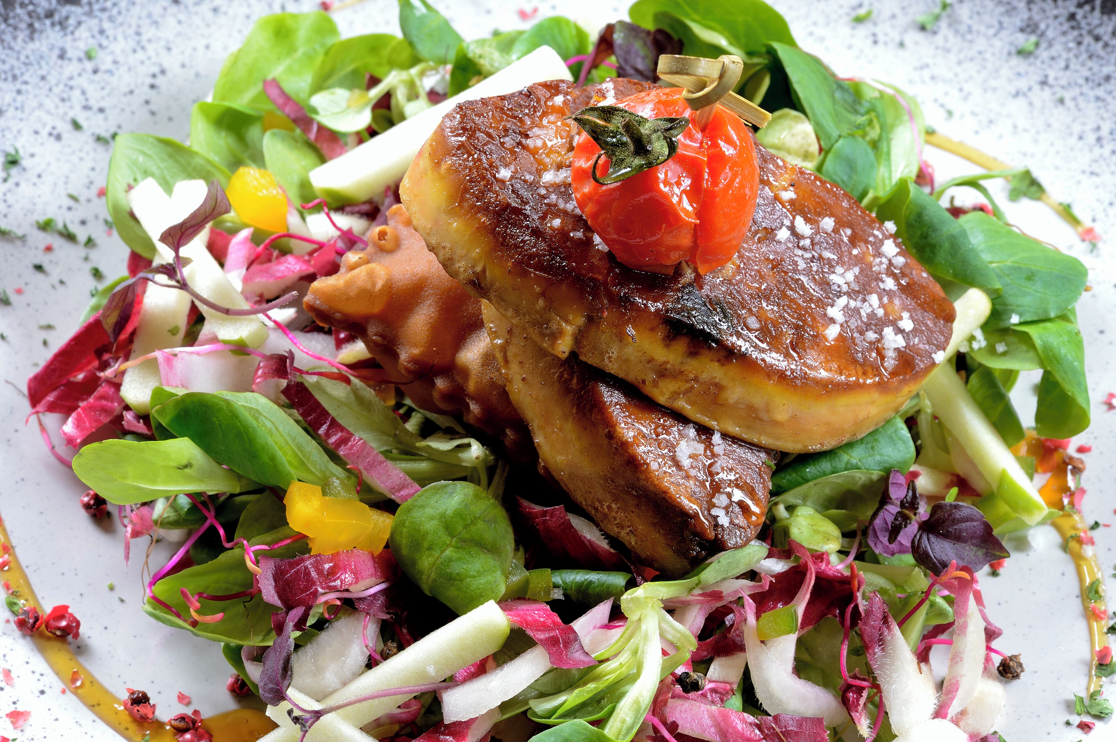 A plate of food with a variety of greens and a grilled item, possibly meat, with a cherry tomato garnish.