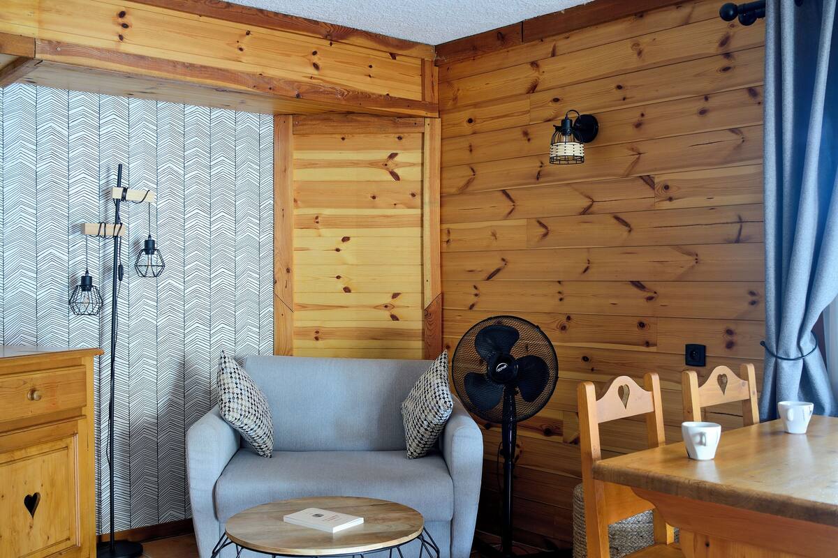 A cozy room with a wooden wall, a sofa, a small table, and a fan.
