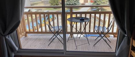 A balcony with a table and chairs, a view of houses and trees, and a wooden railing.