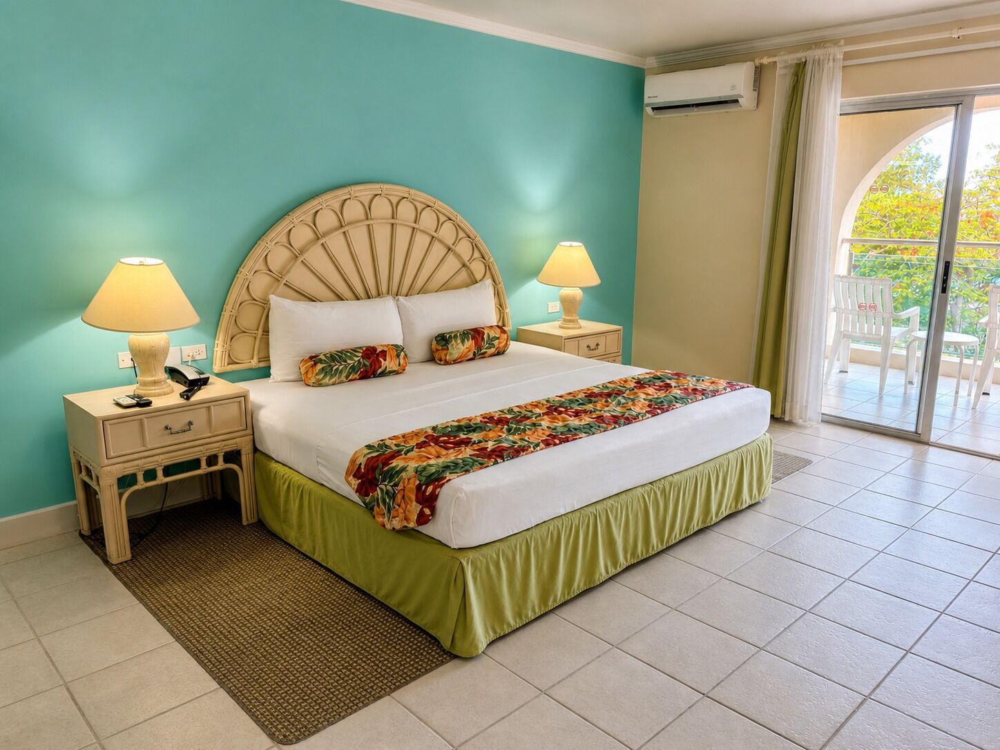 Habitación de hotel con cama, dos mesitas de noche con lámparas, ventana con cortinas y un equipo de aire acondicionado.
