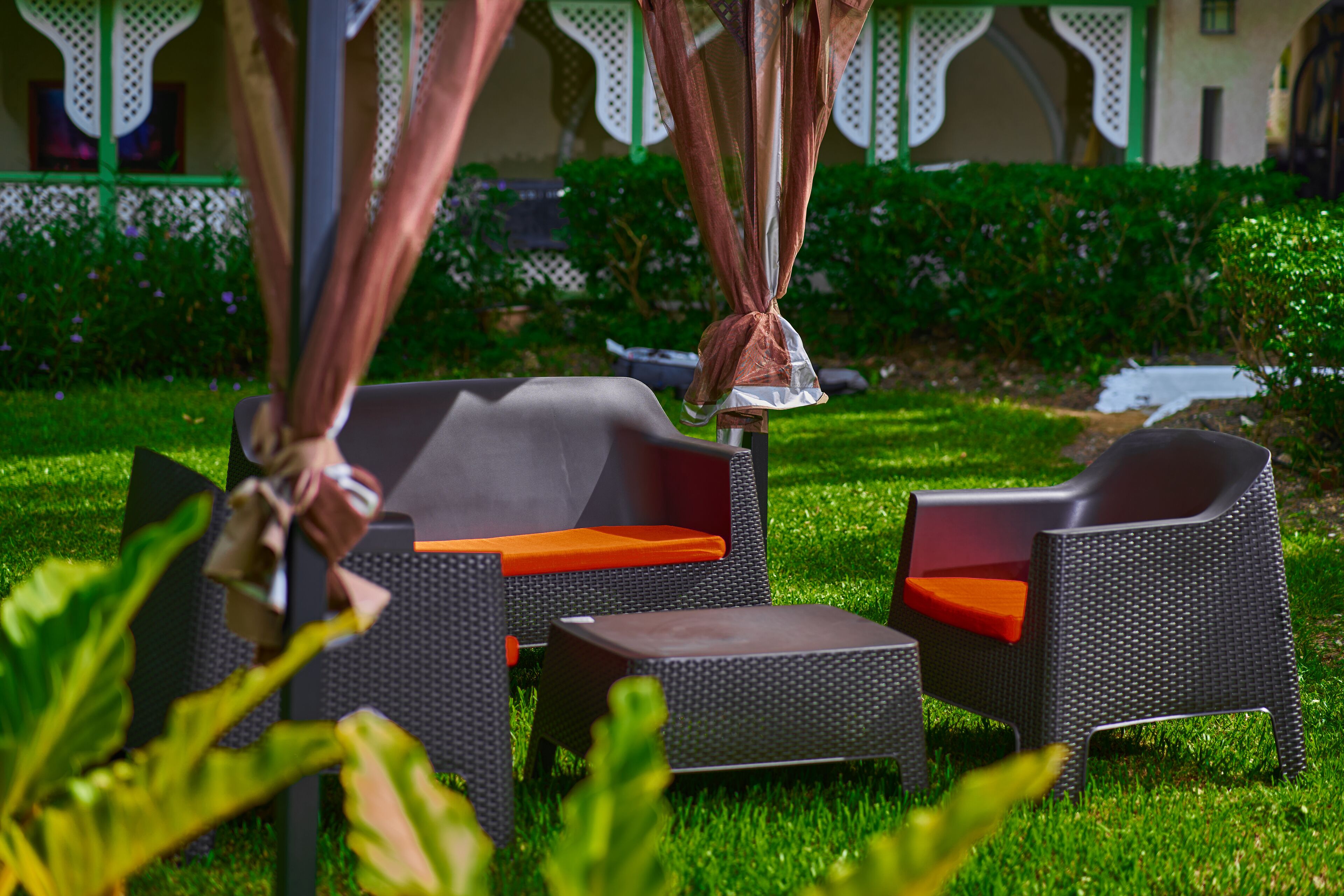Outdoor wicker furniture with orange cushions in a garden setting.