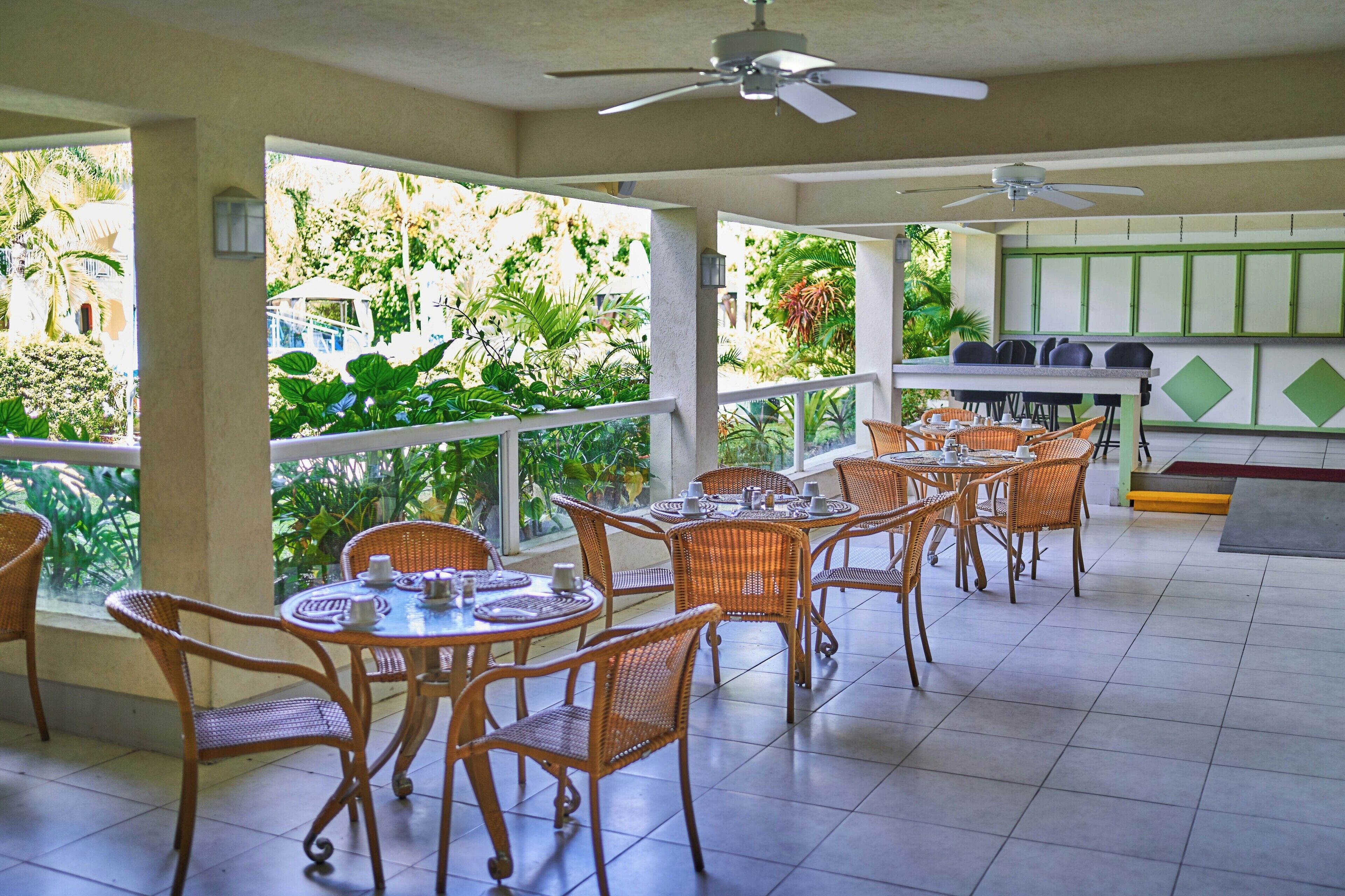 Un espacio de comedor al aire libre techado, con mobiliario de mimbre y vistas a exuberante vegetación.
