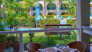 A balcony with wicker furniture and a table set for dining, overlooking a pool and lush greenery.