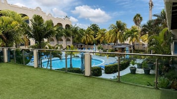Ein Poolbereich mit Palmen, blauem Himmel und einem Gebäude mit Bögen im Hintergrund.