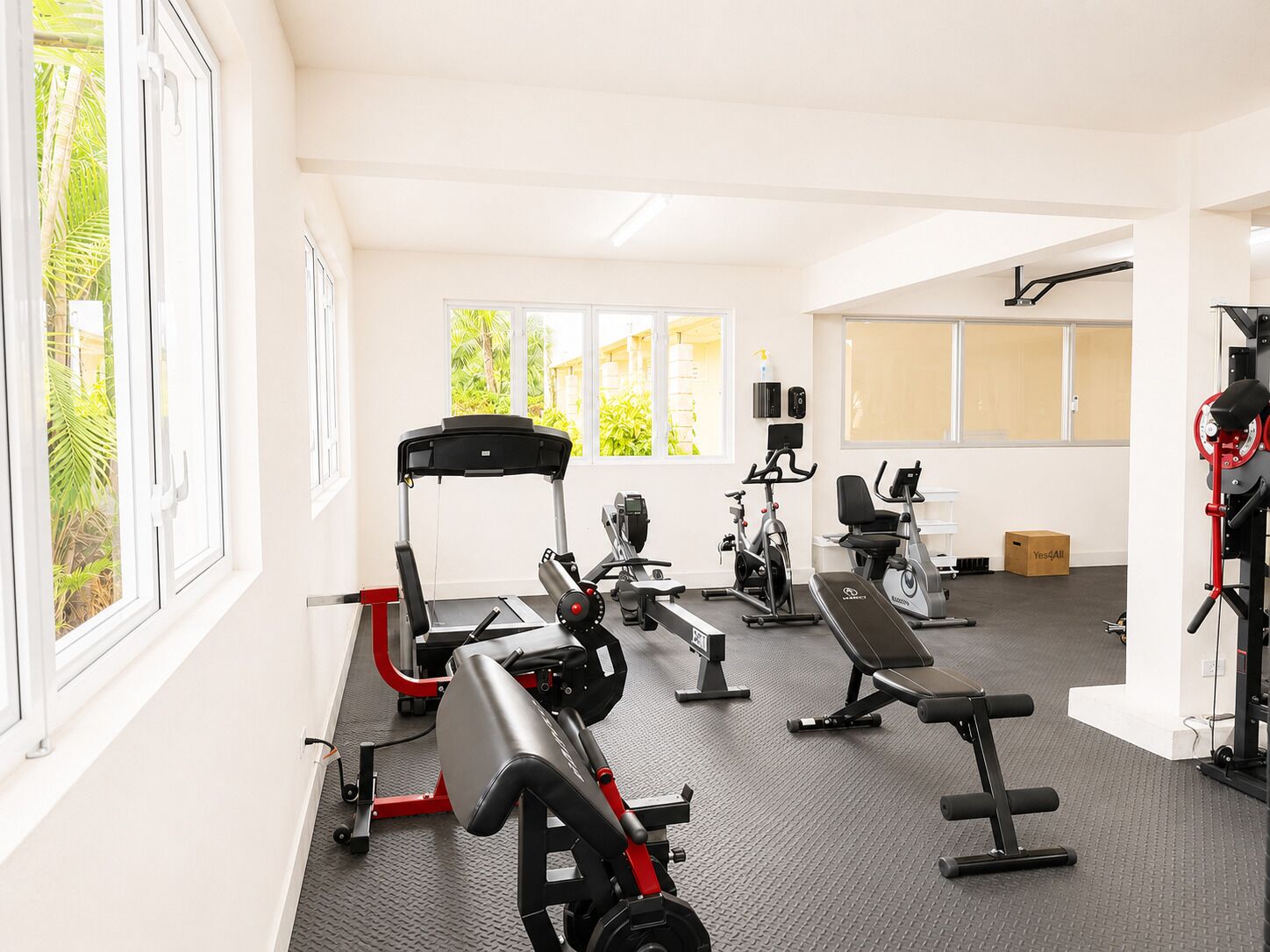 Ein Fitnessstudio mit unterschiedlichen Trainingsgeräten, großen Fenstern und Blick auf Grünflächen.