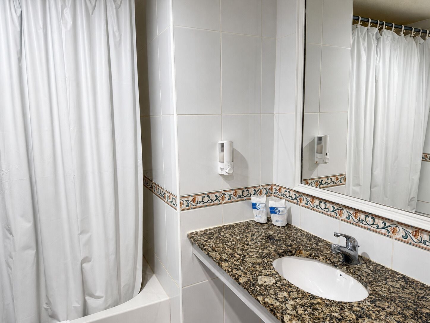 A bathroom with a white sink, a mirror, a shower curtain, and a tiled wall with a decorative border.