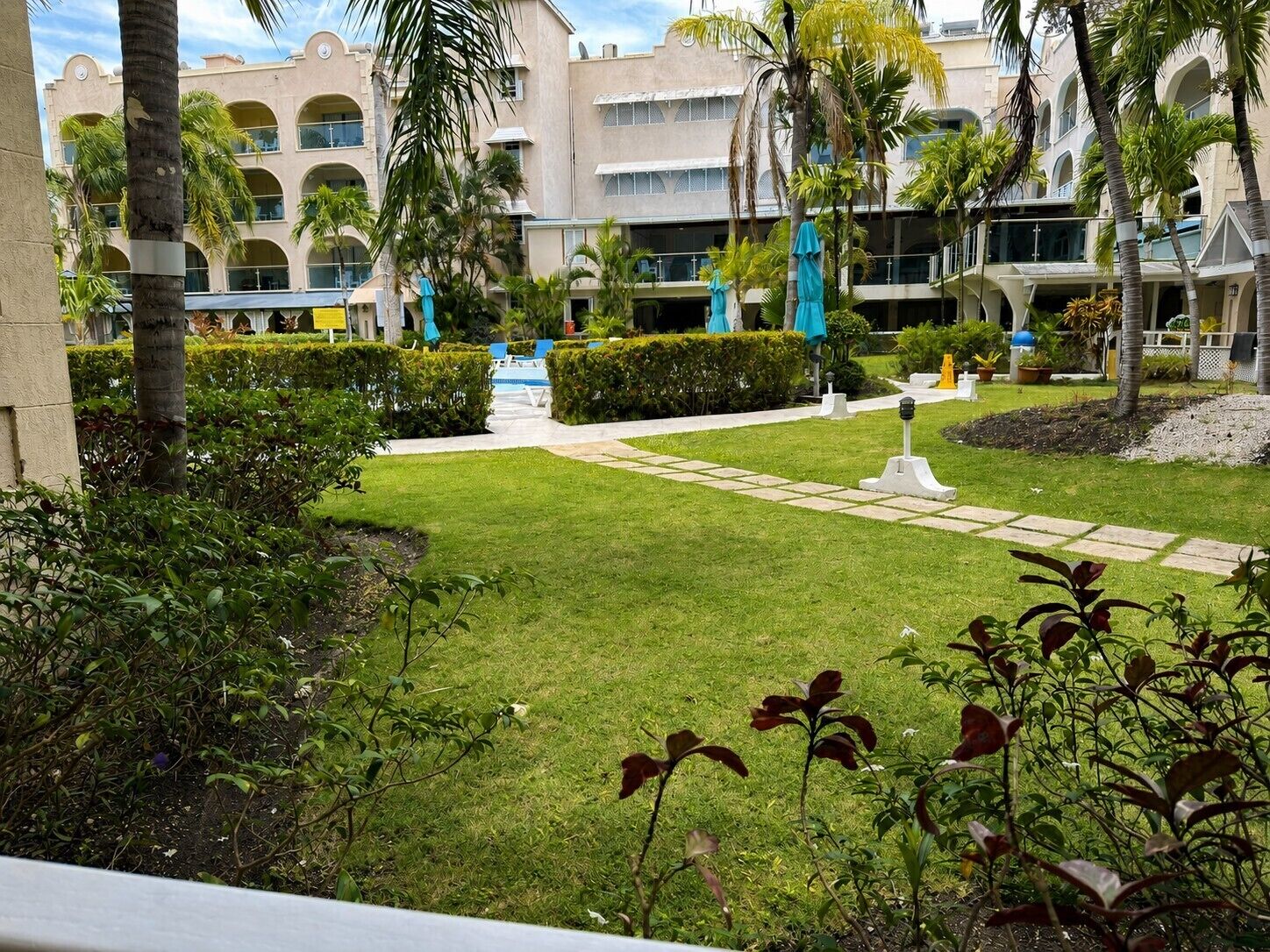 A hotel courtyard with a pool, palm trees, and a well-maintained lawn.