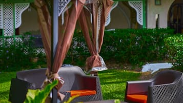 An outdoor seating area with a table and chairs under a canopy, surrounded by greenery.