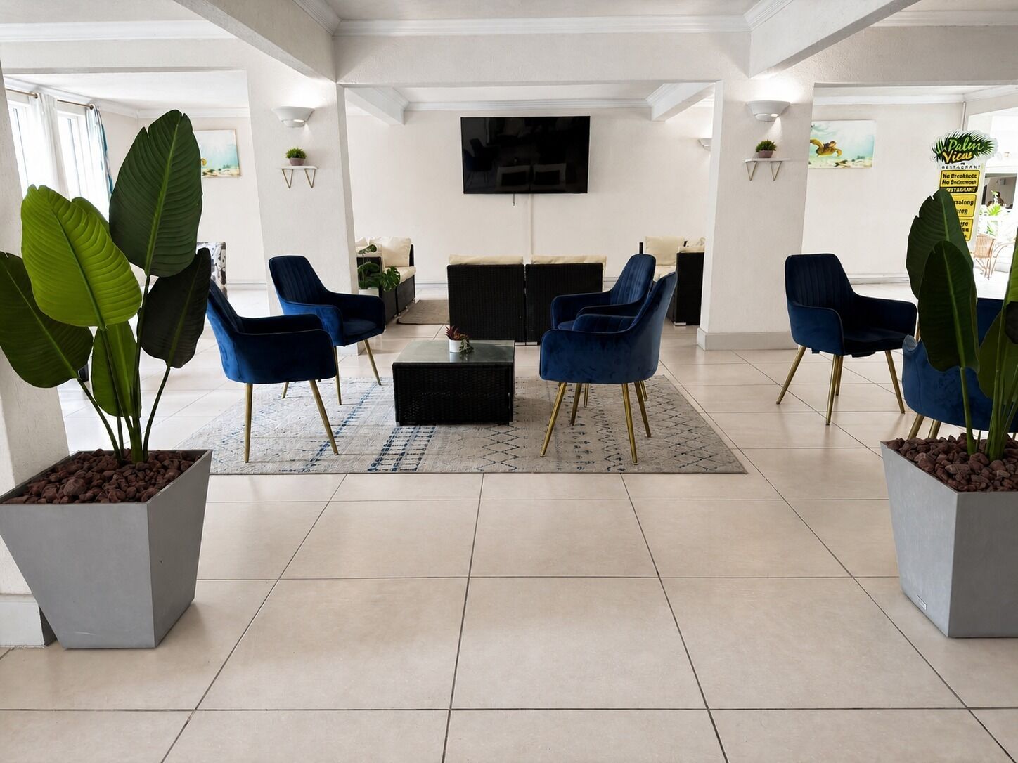 A modern lobby with a seating area, a flat-screen TV mounted on the wall, and potted plants.