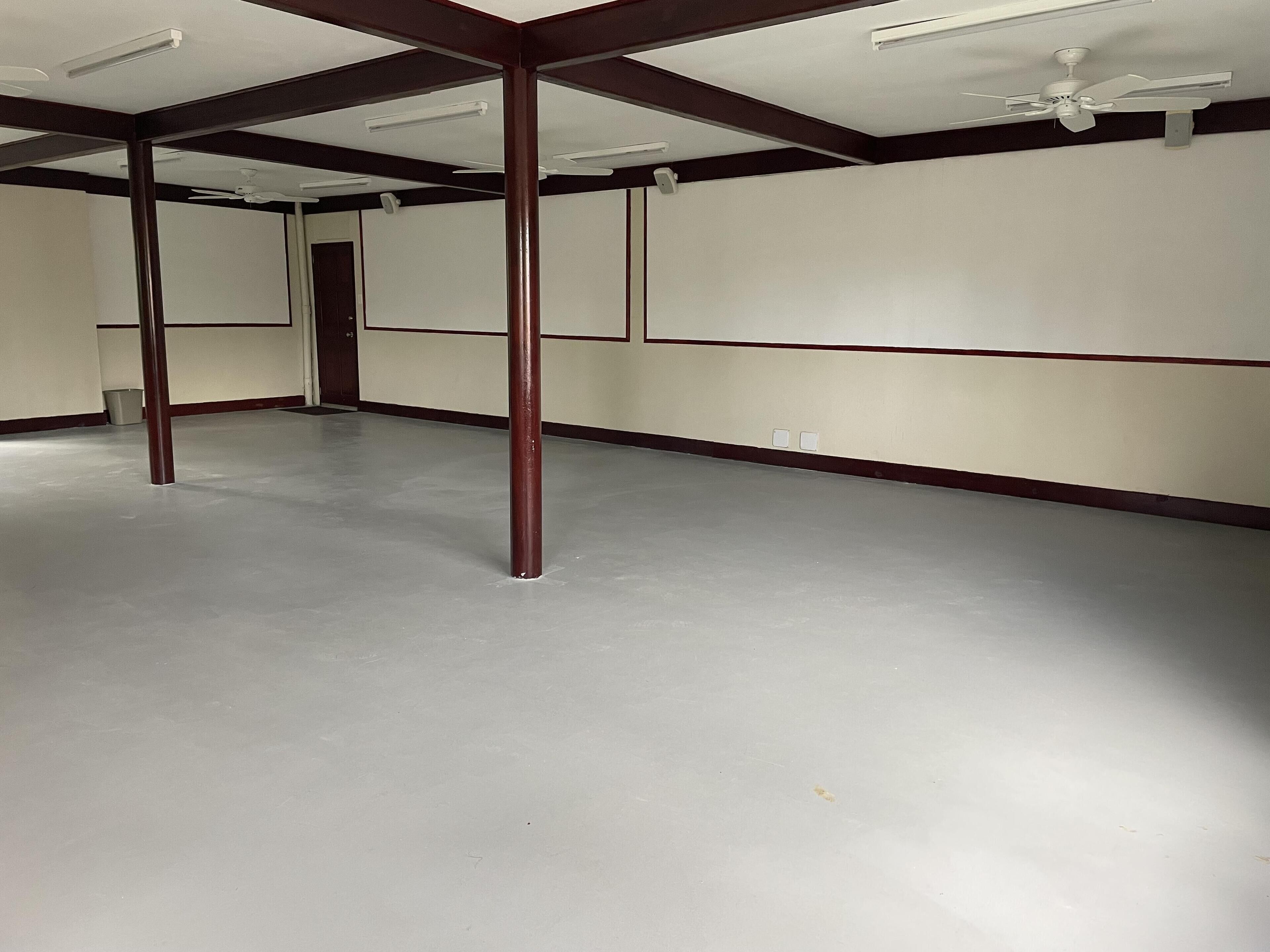 A spacious, empty room with a high ceiling, white walls, and a grey floor.