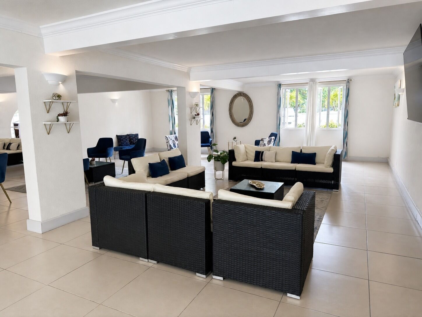 A spacious living area with a black wicker sofa, a cream-colored sofa, and a coffee table. There are two blue chairs and a small table with a plant.
