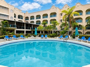 A hotel pool area with a clear blue pool, sun loungers, and palm trees. - Sunbay Hotel (Maxwell)