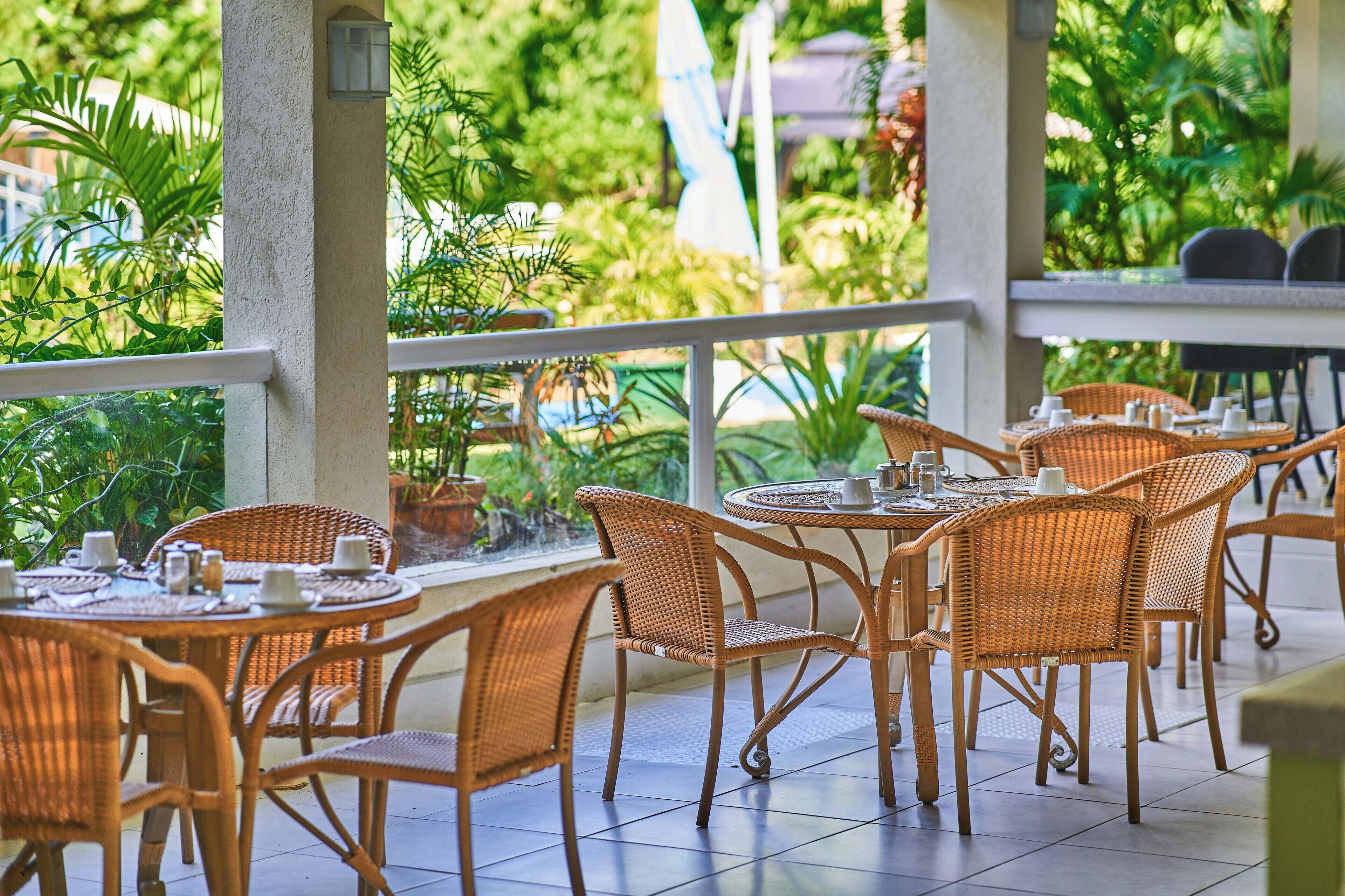A covered outdoor dining area with wicker furniture and potted plants.