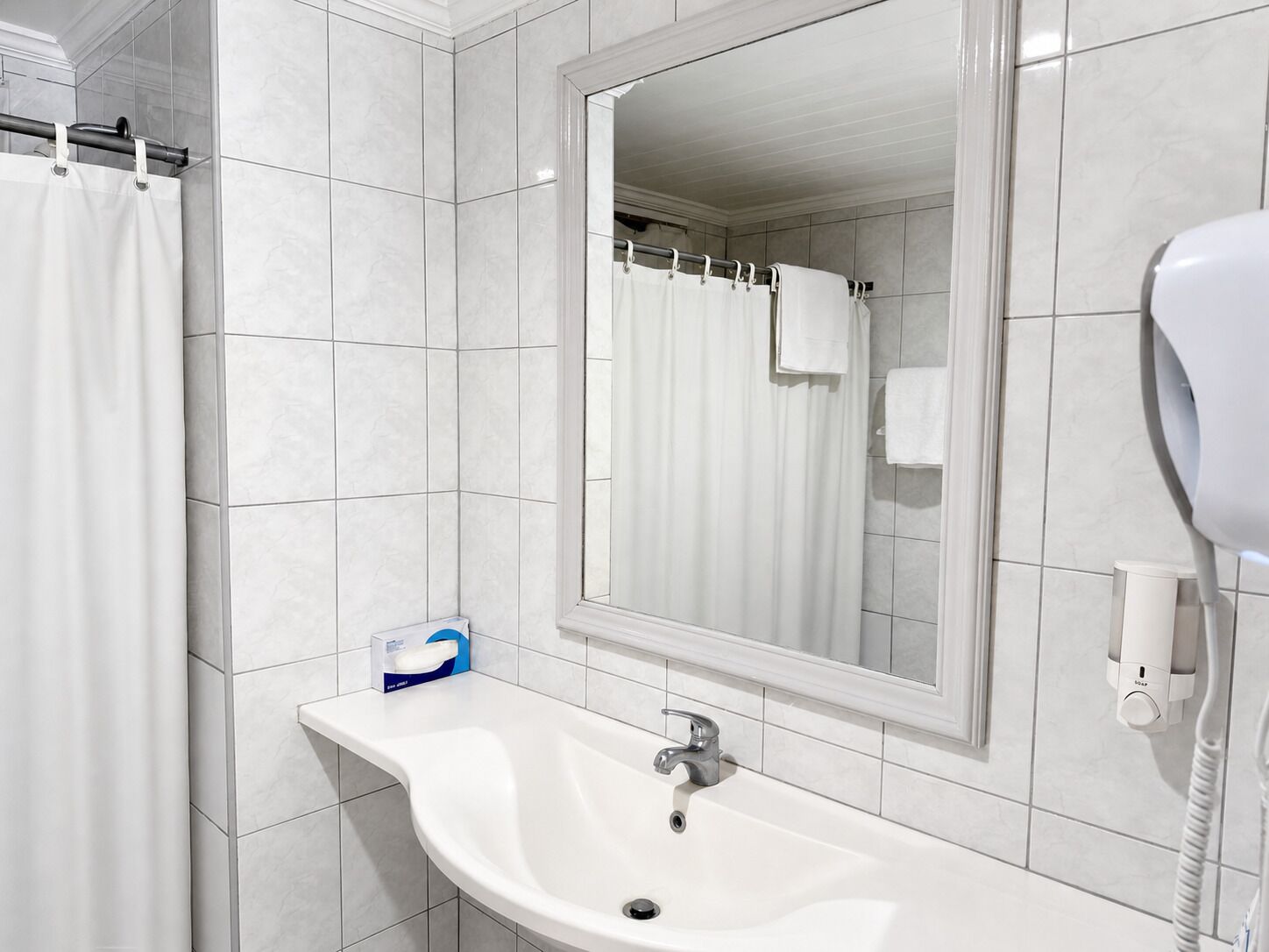 A bathroom with a white sink, a mirror, a shower curtain, and a hairdryer.