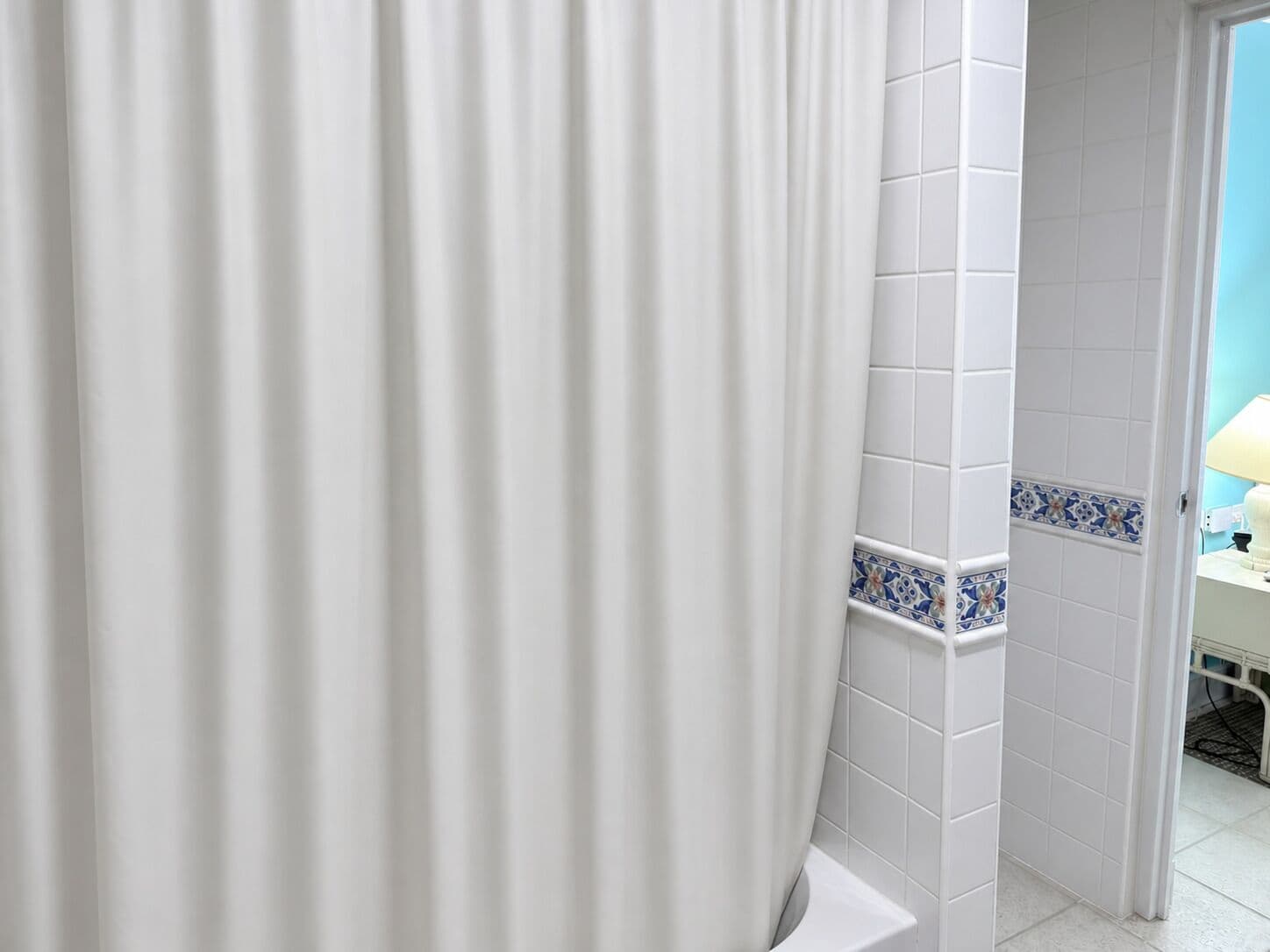 A bathroom with white tiles, a white bathtub, and a blue and white tile border.