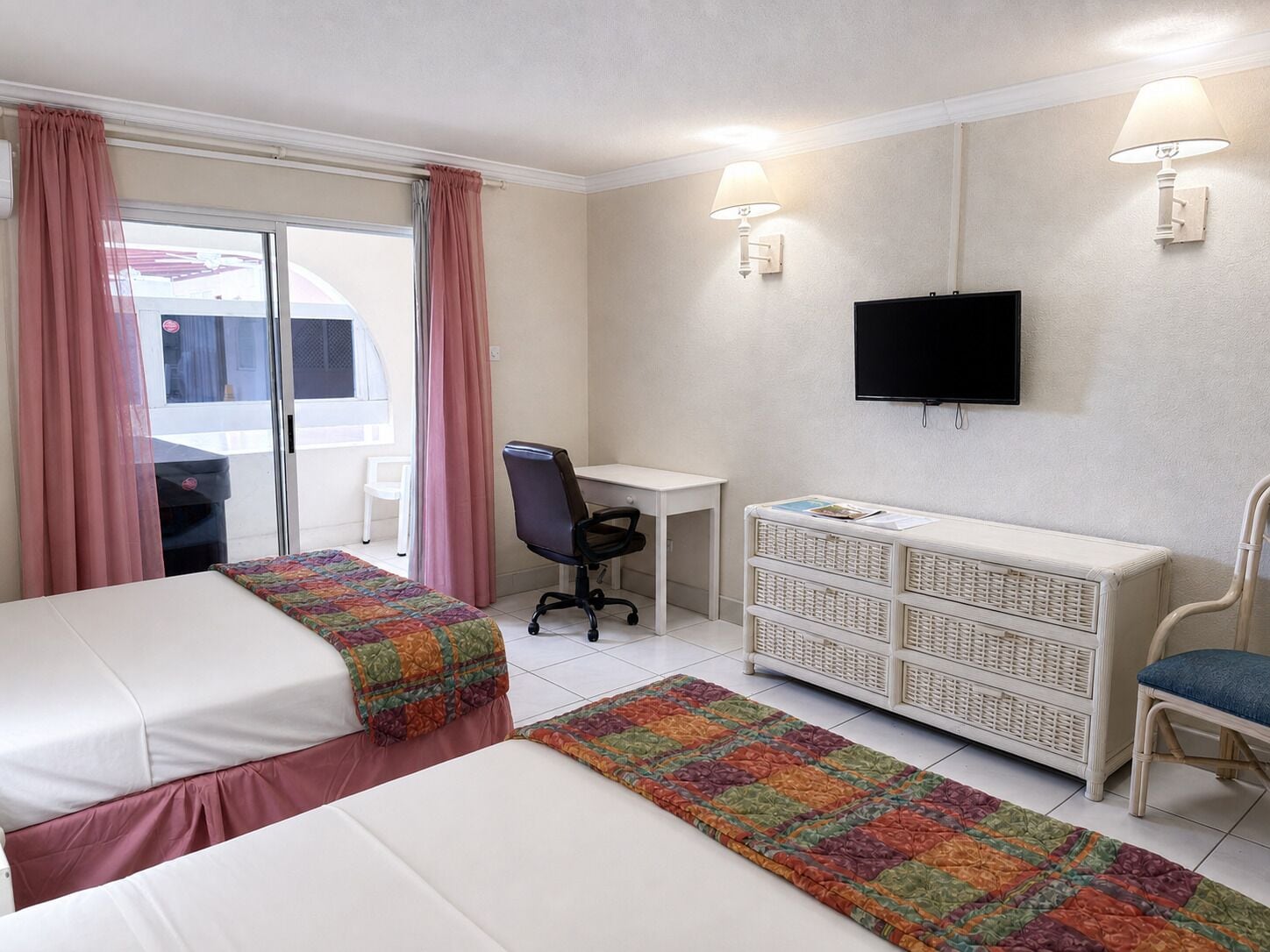 Habitación de hotel con dos camas, un escritorio, una silla, un televisor y una ventana con cortinas.