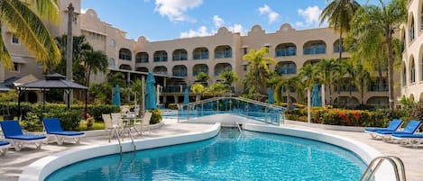 A hotel pool area with a circular pool, lounge chairs, and a building with multiple balconies.