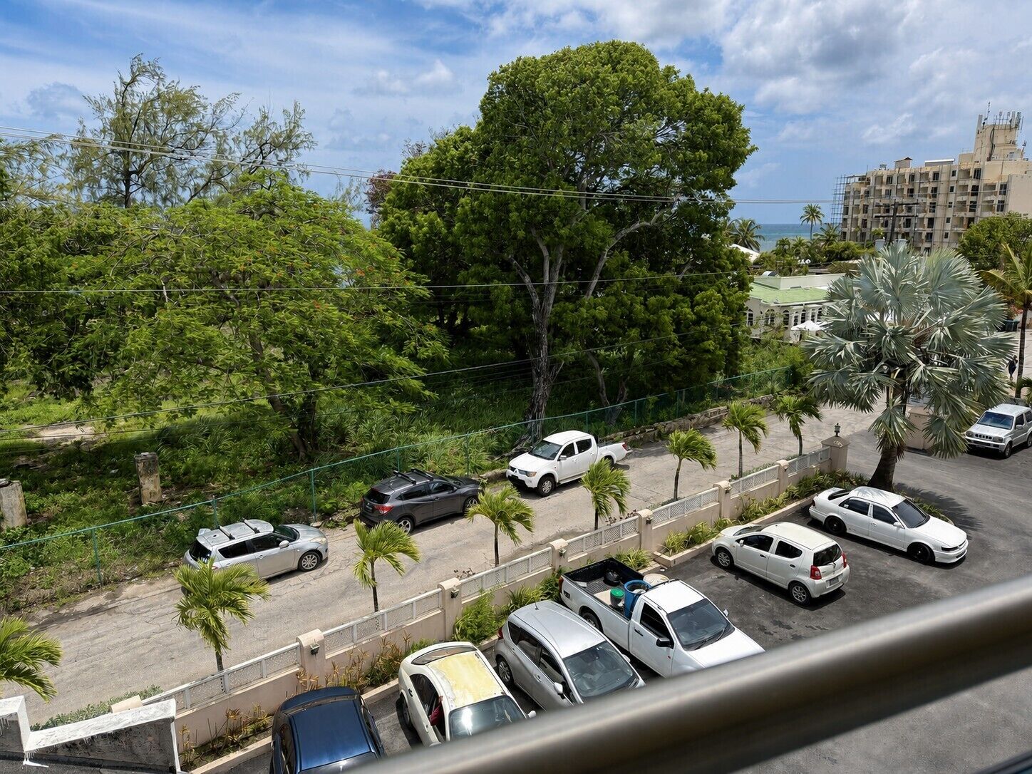 Un’area di parcheggio con diverse auto, un edificio sullo sfondo e un albero in primo piano.
