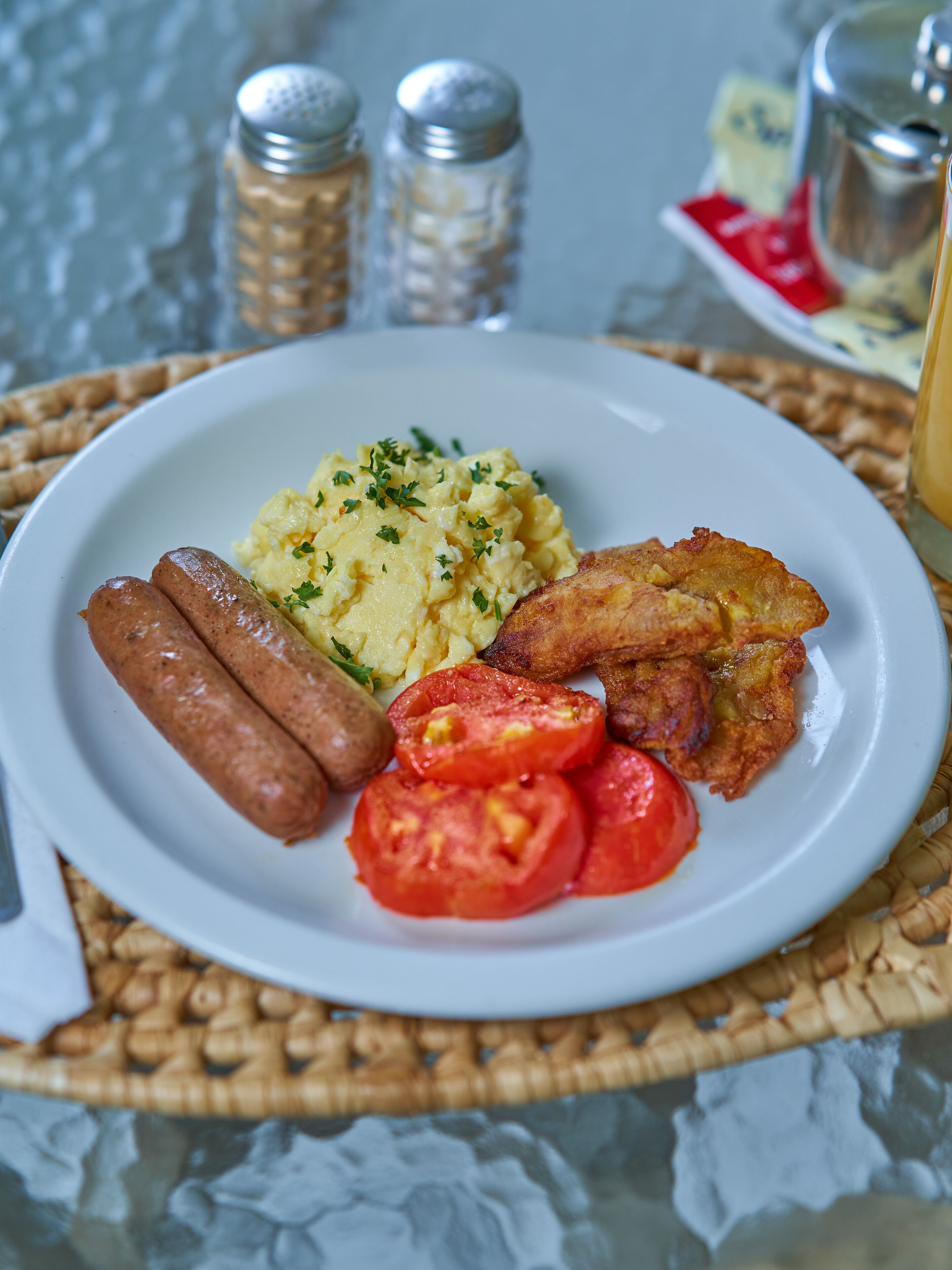 A plate of food with sausages, scrambled eggs, fried potatoes, and tomatoes.
