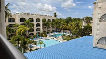 A hotel with a swimming pool surrounded by palm trees and lounge chairs.