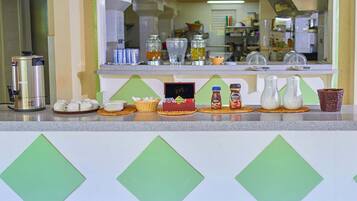 A breakfast bar with coffee makers, condiments, and a cake.
