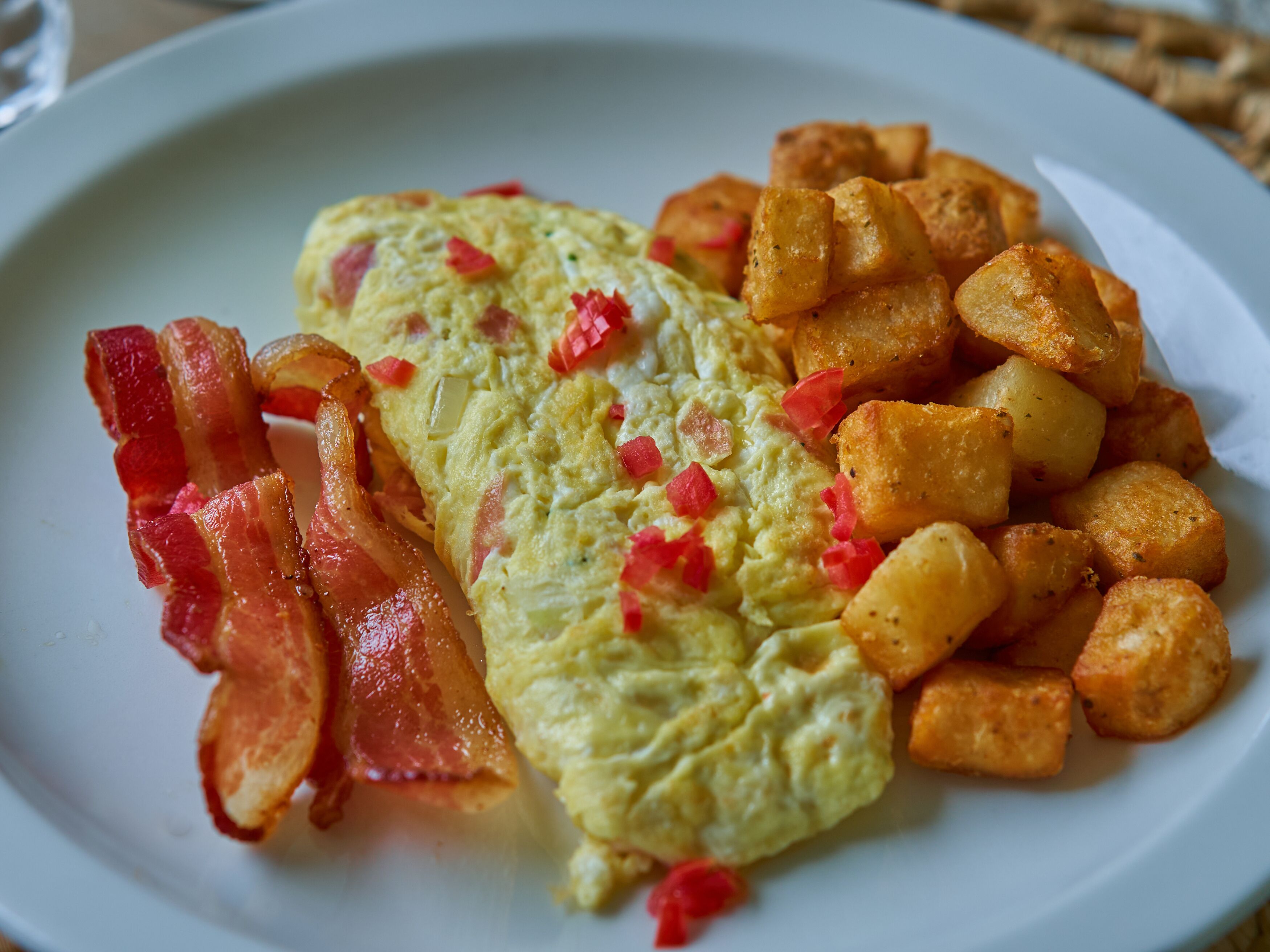 A plate with an omelette, bacon, and roasted potatoes.