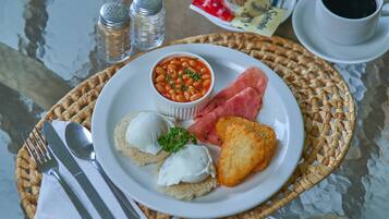 Un piatto con fagioli, prosciutto, pane tostato e una tazza di caffè su un tavolo con saliera e pepiera.