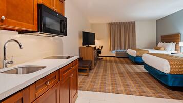 Una habitación de hotel con kitchenette, televisión, cama y escritorio.