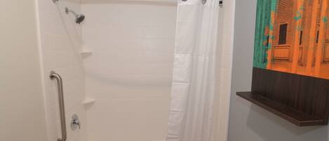 A bathroom with a white bathtub, a shower with a handheld showerhead, a grab bar, and a white curtain.
