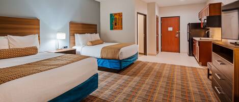 A hotel room with two beds, a desk, a TV, and a bathroom door.