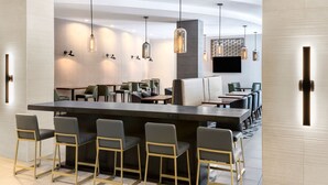 Un espace repas moderne doté d’un long bar, de plusieurs options d’aménagement pour s’asseoir, d’un éclairage suspendu et d’un téléviseur à écran plat fixé au mur.