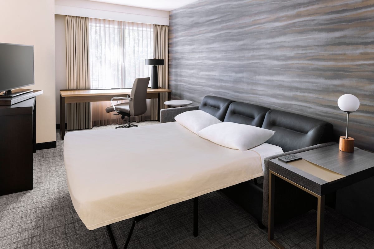 Une chambre d’hôtel avec un grand lit, un bureau avec une chaise, une télévision et une lampe.