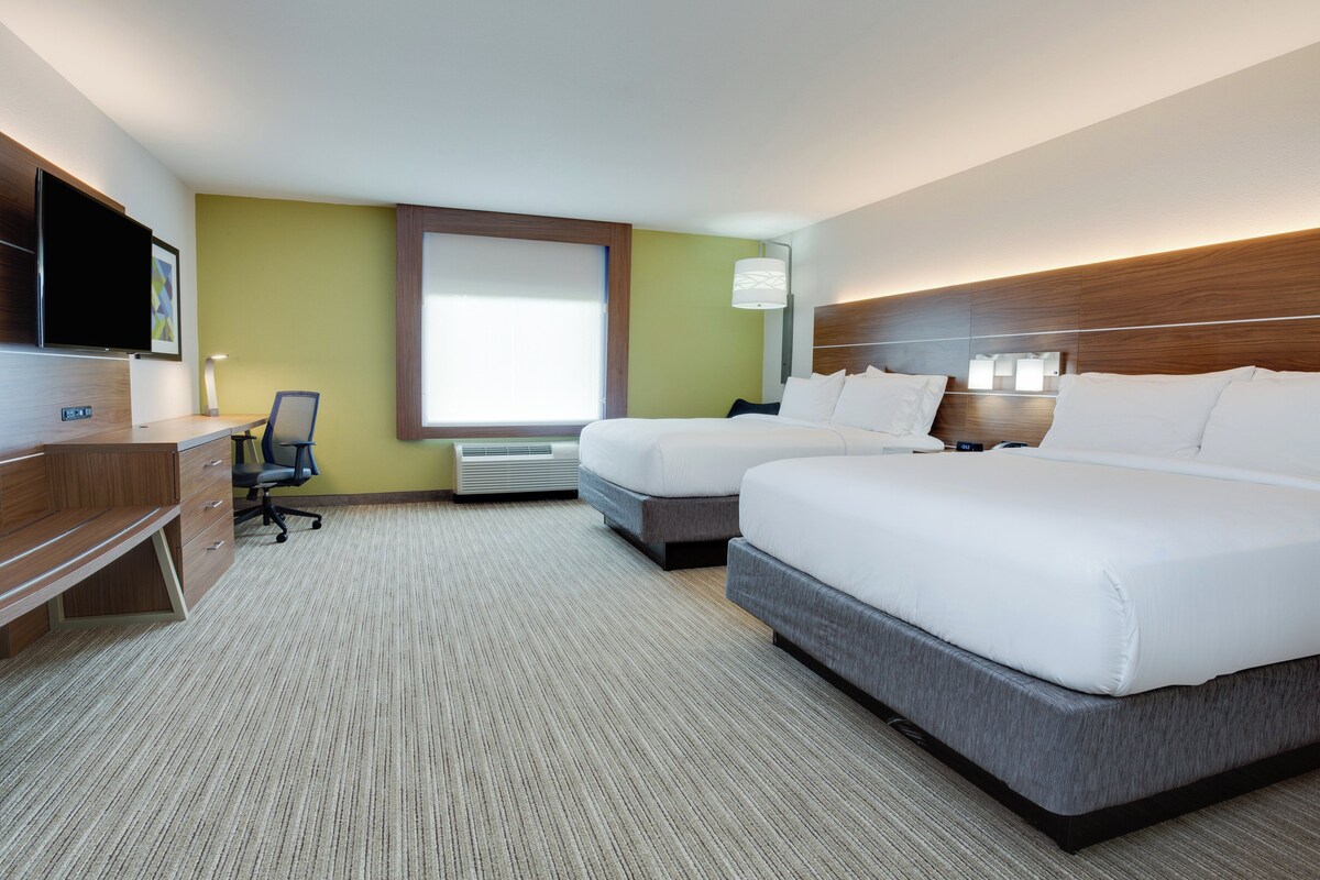 A hotel room with two beds, a desk, a chair, a TV, and a window.