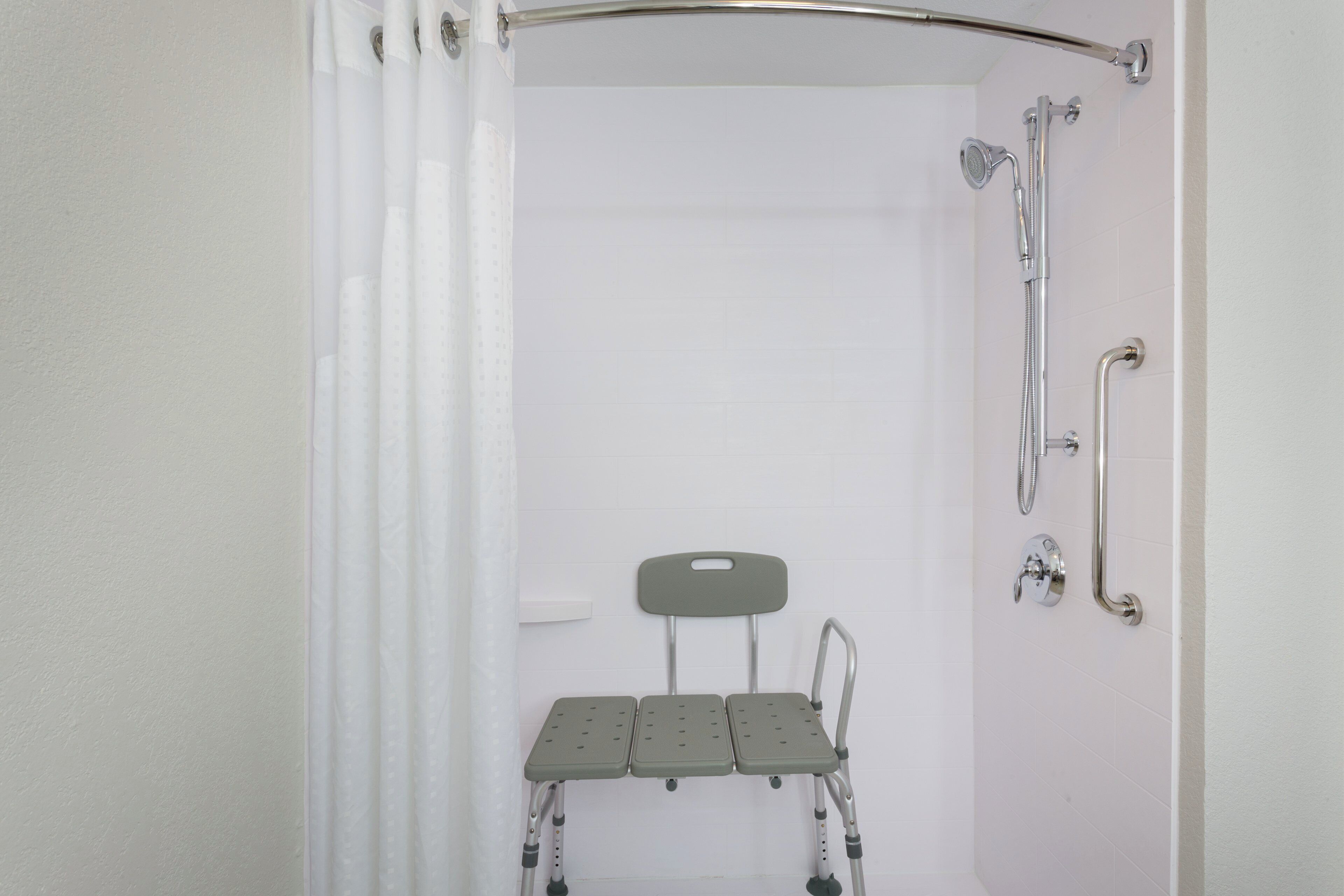A shower area with a shower chair, grab bars, and a shower head.