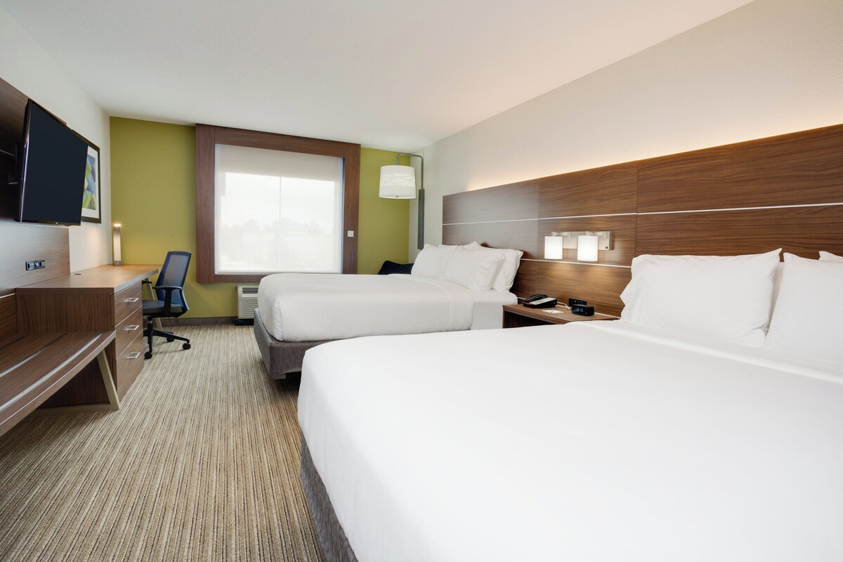 A hotel room with two beds, a desk, a chair, a TV, and a window.