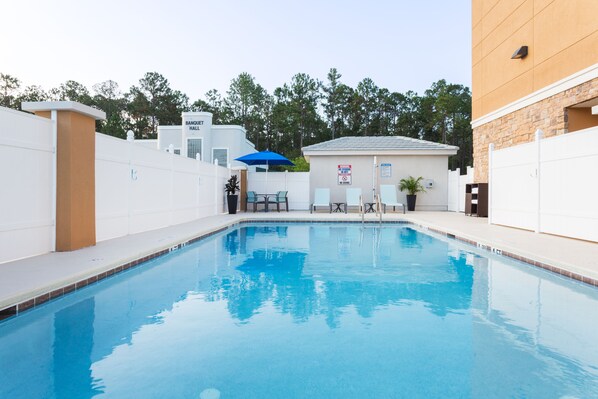 Une piscine avec un parasol bleu, un espace de repos couvert et, au fond, un bâtiment portant l’inscription « SALLE DE BANQUET ».