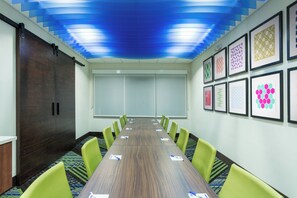 Ein Konferenzraum mit einem langen Tisch, grünen Stühlen und gerahmten Kunstwerken an den Wänden.