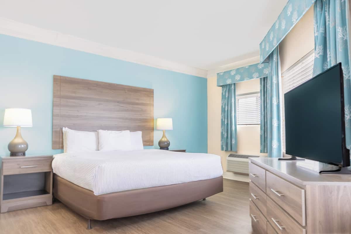 Une chambre d’hôtel avec un lit, des lampes de chevet, une commode, une télévision et une fenêtre avec des rideaux.
