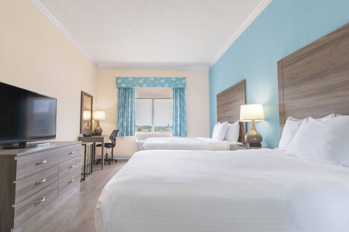 Een hotelkamer met twee bedden, een televisie, een bureau en een raam met gordijnen.