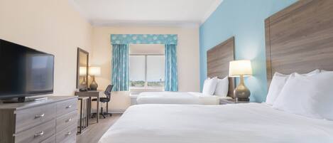 Habitación de hotel con dos camas, televisión, escritorio y ventana con cortinas.