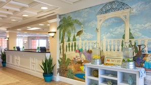 Zona de recepción de hotel con un mural, un mostrador de recepción, plantas en macetas y un letrero que dice 'Today's Catch'.