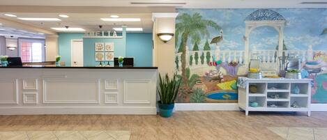 A reception area with a counter, a mural, and a potted plant.