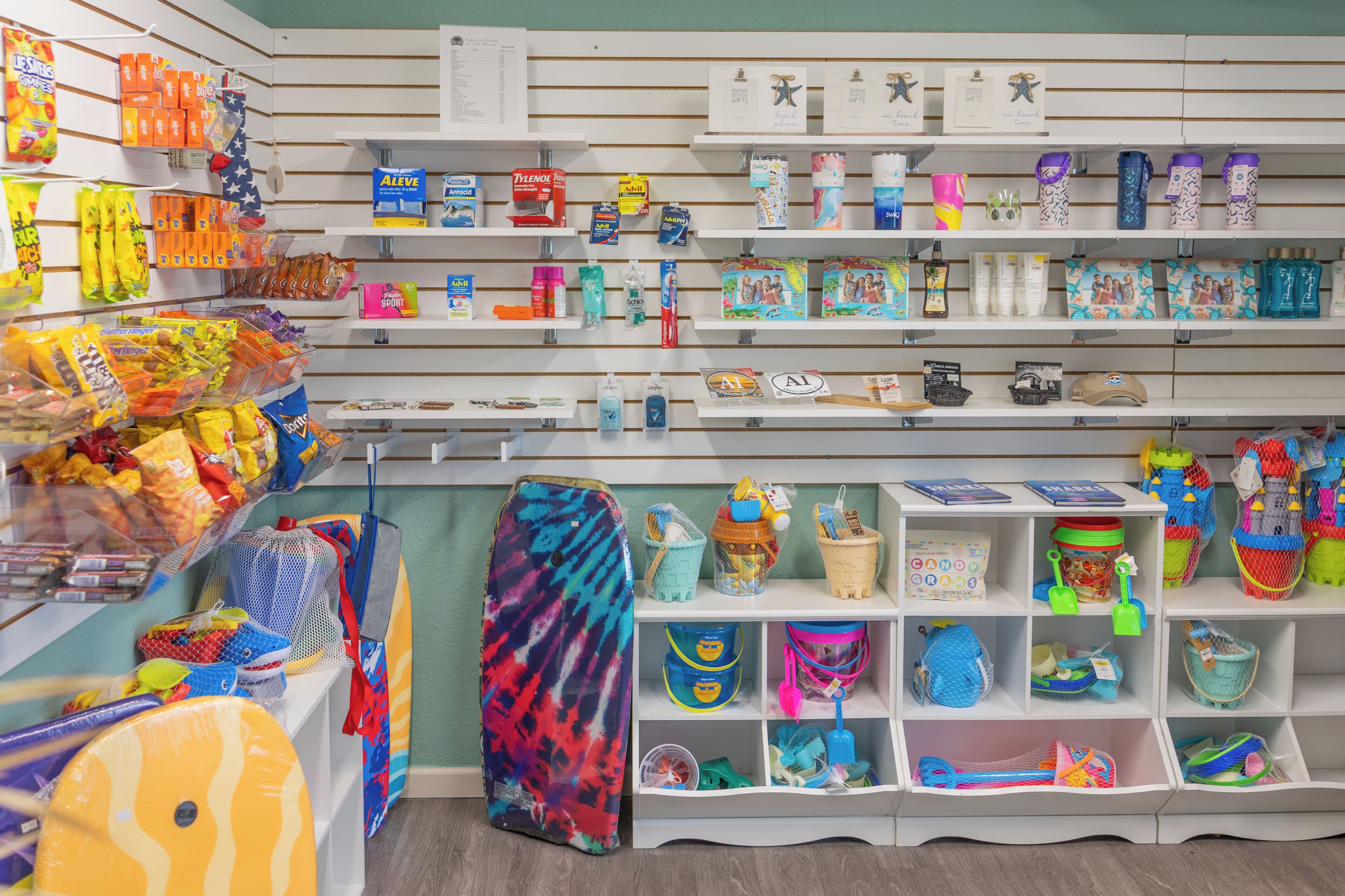 Una tienda con estantes llenos de diversos productos, como bocadillos, artículos de aseo personal y complementos para la playa.